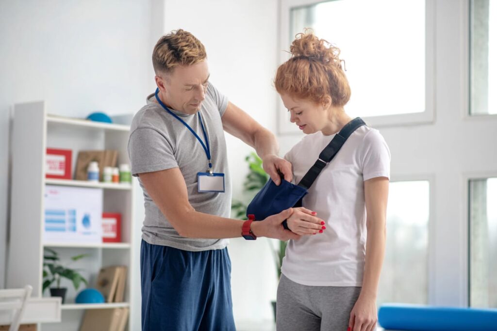 An auto accident chiropractor examines a woman with her arm in a sling.